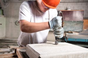 Typische Arbeitssituationen von Betonwerkern: Auszubildender bearbeitet die Oberfläche eines Betonselements mechanisch, um der Oberfläche eine Struktur zu verleihen.