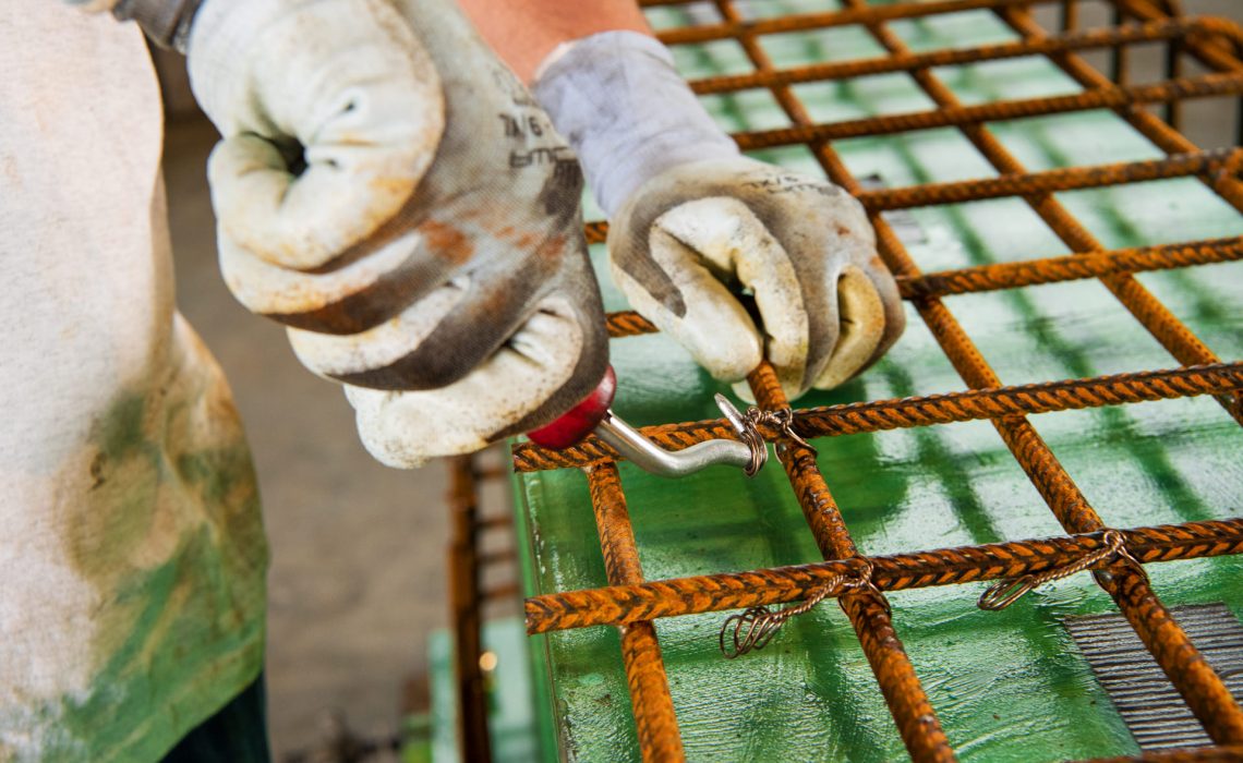 Typische Arbeitssituationen von Betonwerkern: Auszubildender befestigt Draht an Schalungsgitter.